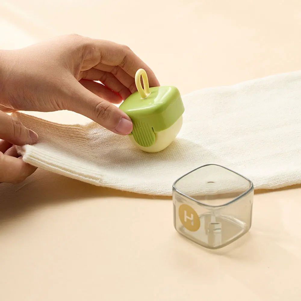 Hand holding a small green and white Lint remover container on a beige surface with a glass container in the foreground.