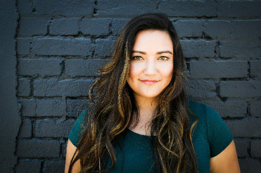 Woman with long dark hair wearing a green shirt against a dark brick wall.